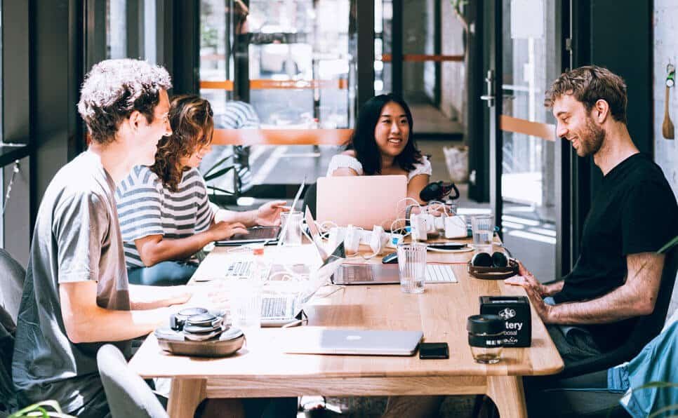 Four colleagues working together at a co-working space with laptops and notebooks.