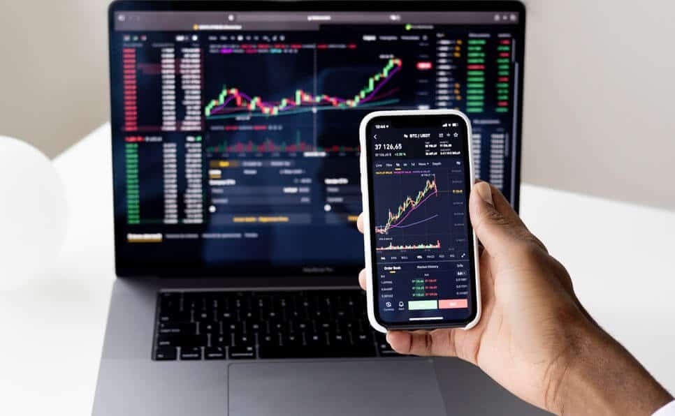 Person monitoring financial charts on a laptop and smartphone.