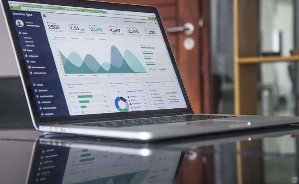 A laptop on a glass table displaying financial data and graphs.