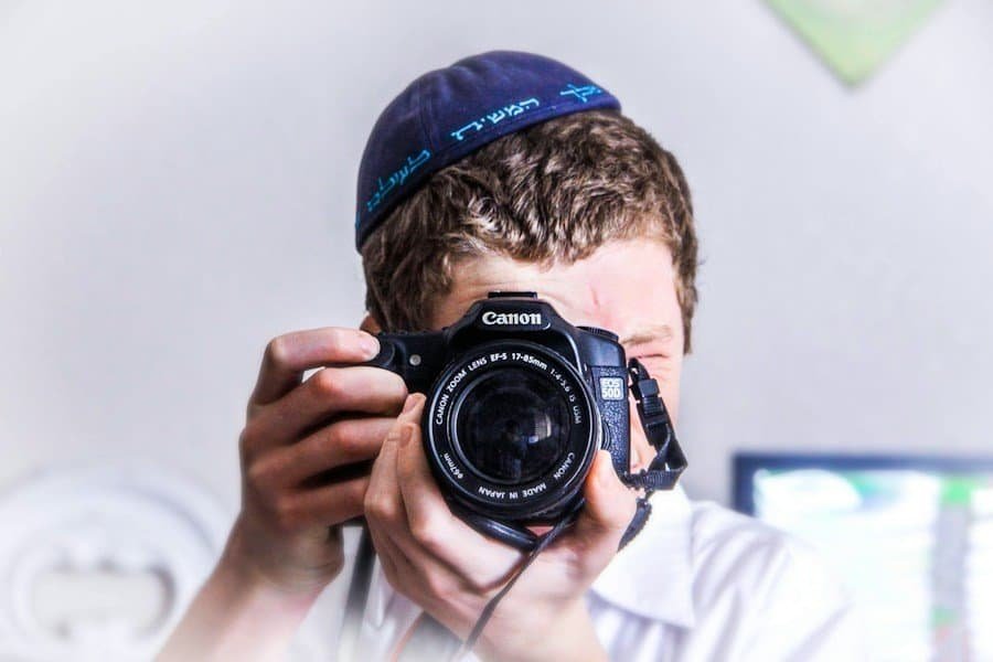 Person holding a canon dslr camera up to their face, taking a photograph.