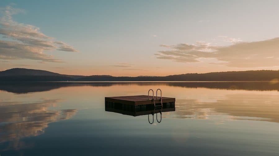 A tranquil lake at sunset with a floating dock and reflective water surface.