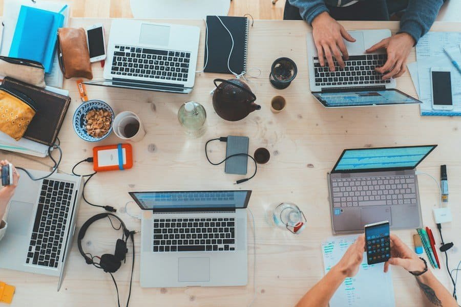 Four individuals working at a table with laptops, mobile devices, and snacks.