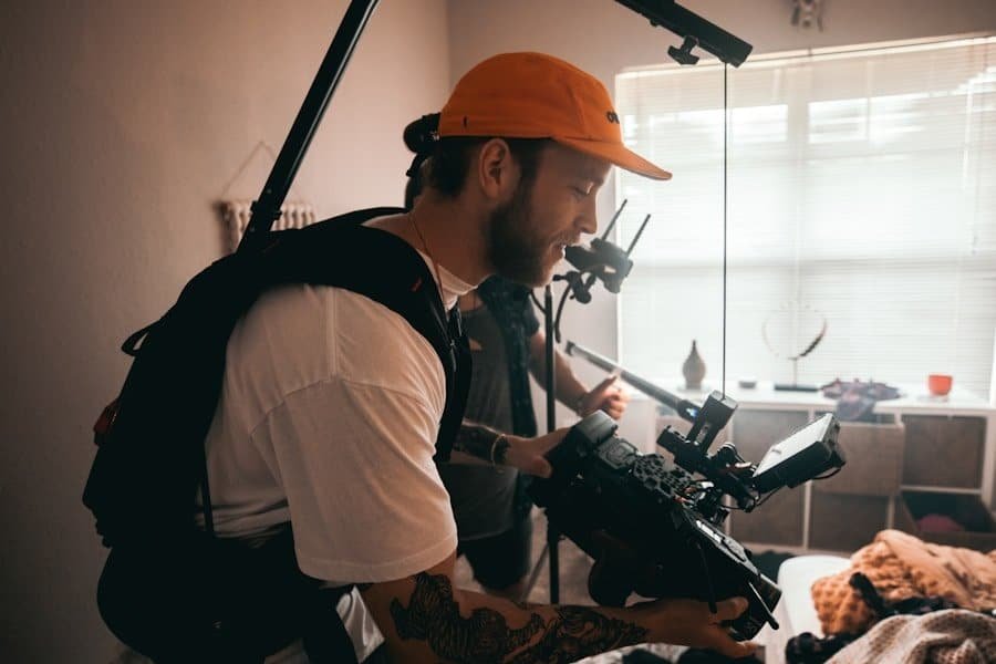 A man with a baseball cap operates a handheld camera rig indoors.