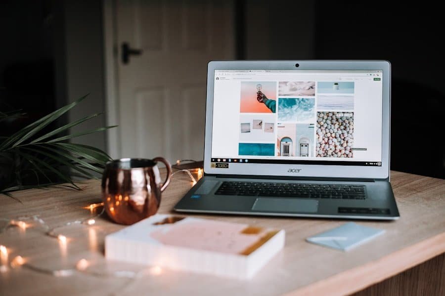 A laptop displaying a mood board on the screen, placed on a table with a copper mug, string lights, and a notebook.